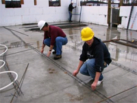 Workers installing tubing over concrete subfloor.